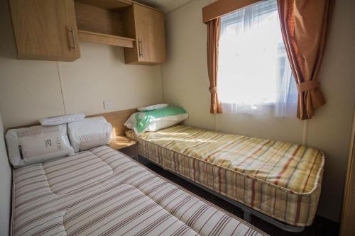 two beds in a small room with a window at Lovely Caravan With Free Wifi Nearby Great Yarmouth Seaside Town Ref 20085bs in Hopton on Sea