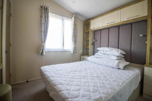 a bedroom with a large white bed with a window at Beautiful 6 Berth Caravan At Suffolk Sands Holiday Park Ref 45010mv in Felixstowe
