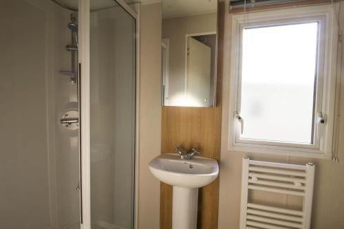 a bathroom with a sink and a mirror and a window at Lovely 6 Berth Caravan At Coopers Beach Park In Essex Ref 49075p in East Mersea