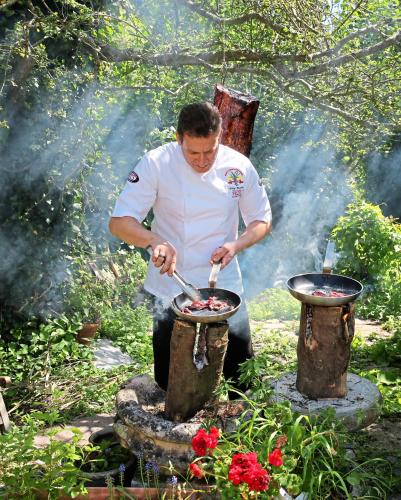 a man cooking food in a pot on a grill at Saints Bay Hotel in St Martin Guernsey