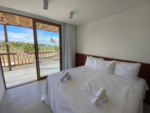 Cette chambre comprend un lit avec des draps blancs et une grande fenêtre. dans l'établissement Casa Seriguela - Praia do Patacho - Rota Ecológica dos Milagres, à Porto de Pedras