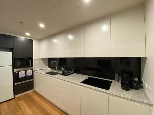 a kitchen with white cabinets and black appliances at New 2 Bed 2 Bath Apt at The Heart of Canberra - 2 Car Spaces in Canberra