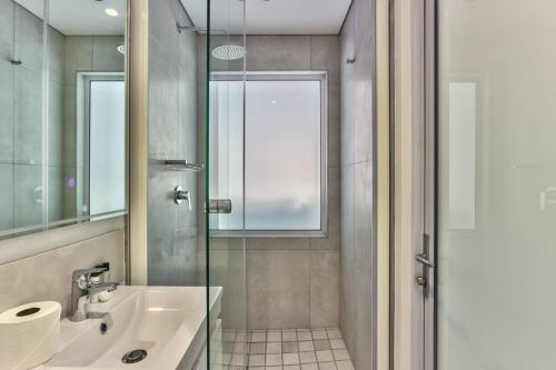 ein Bad mit einem Waschbecken und einer Glasdusche in der Unterkunft Contemporary arty Studio Balcony Mountain views in Kapstadt