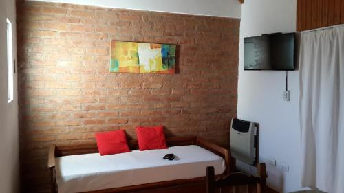 Habitación con cama con almohadas rojas y pared de ladrillo. en Guardalaola en Las Grutas