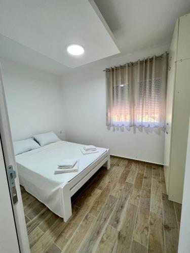 a white bedroom with a bed and a window at Relax Apartmani in Sutomore