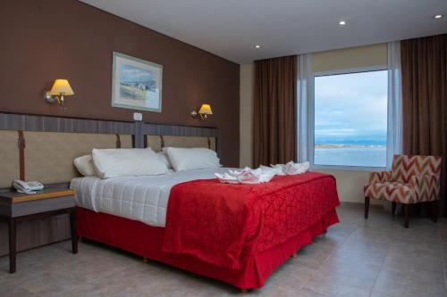 a hotel room with a bed with a red blanket and a window at Hotel Las Dunas in El Calafate