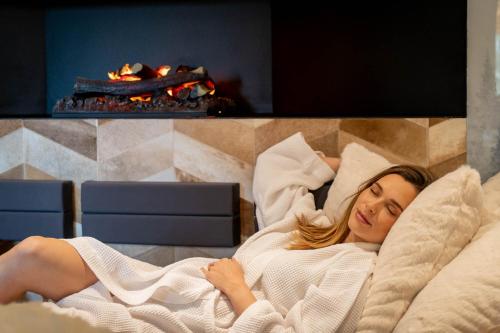 a woman laying in a bed in front of a fireplace at Domaine Des Hautes Fagnes in Ovifat