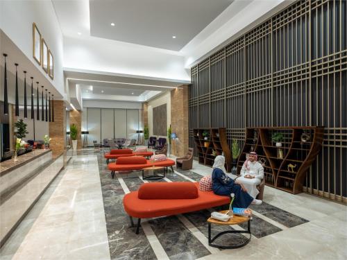 two people sitting on orange chairs in a lobby at Novotel Makkah Thakher City in Makkah