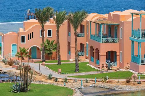 a pink house with palm trees in front of the ocean at Radisson Blu Resort El Quseir in Quseir