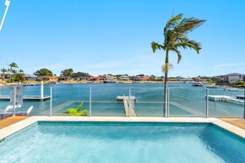 a swimming pool with a palm tree and a body of water at Sandy Shores - Absolute Waterfront & Swimming pool - Holiday Yamba in Yamba