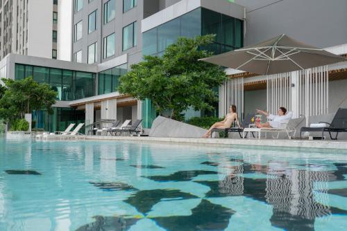 twee personen zitten onder een parasol naast een zwembad bij Holiday Inn & Suites Siracha Laemchabang, an IHG Hotel in Si Racha