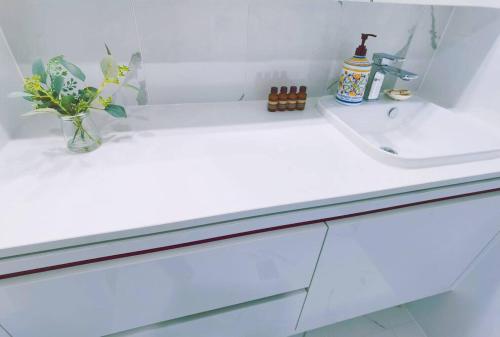 a white bathroom counter with a sink and a vase of flowers at Brand New PARK AVENUE Apartment in the Heart of Canberra City in Canberra