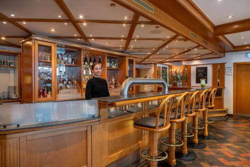 a woman standing behind a bar with stools at Hotel Elisenhof Mönchengladbach in Mönchengladbach