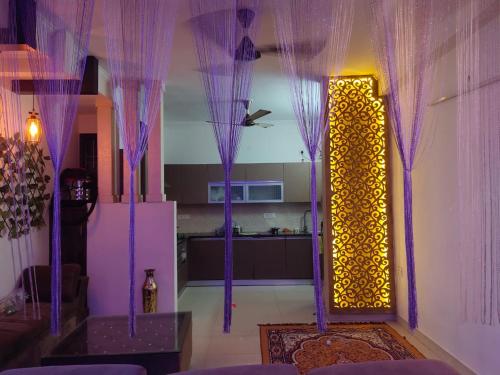 a living room with purple curtains and a kitchen at Own Stay in New Delhi