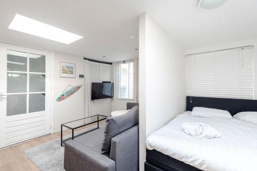 ein Schlafzimmer mit einem Bett, einem Sofa und einem TV in der Unterkunft Garden Cottage in Zandvoort