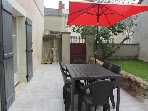 a wooden table with chairs and a red umbrella at Gîte Saumurois 7 personnes in Montreuil-Bellay