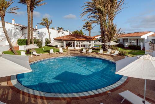 a swimming pool with umbrellas and palm trees at AluaSun Mediterráneo in S'Algar