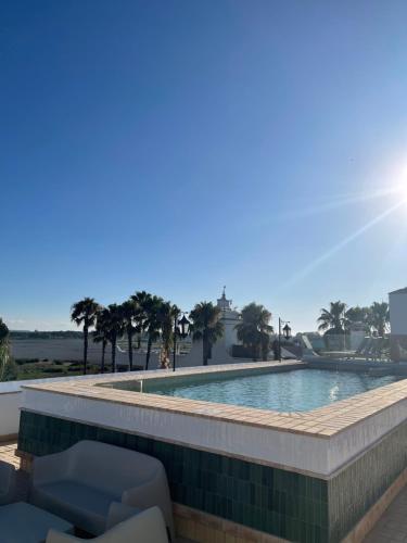 a swimming pool with chairs and palm trees at Hotel La Malvasía in El Rocío