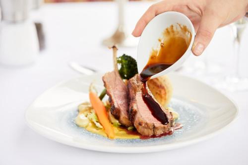 a person is pouring sauce on a plate of food at Ednam House Hotel in Kelso