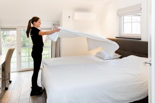 a woman is making a bed in a room at Hof van Salland Hellendoorn in Hellendoorn