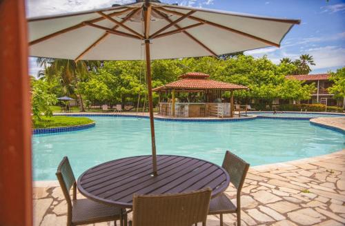 a table with an umbrella in front of a swimming pool at Angá Beach Hotel in São Miguel dos Milagres