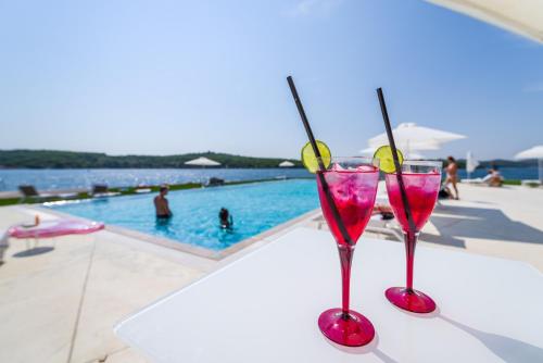 two martini glasses sitting on a table next to a swimming pool at D-Resort Šibenik in Šibenik