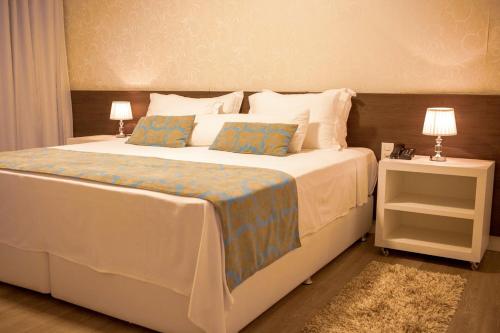 um quarto com uma grande cama branca e 2 candeeiros em Hz Hotel em Patos de Minas