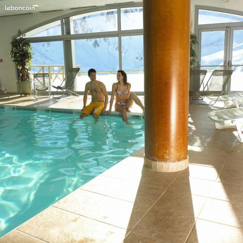 2 personnes assises au bord d'une piscine dans l'établissement Comfort Duplex Apartment, Foot Of The Slopes, à Bagnères-de-Bigorre