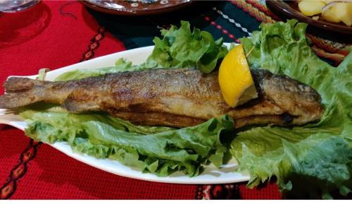 un plato de pescado con lechuga y un limón en él en Къща за гости Динас en Zmeitsa