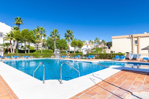 a swimming pool at a resort with chairs and palm trees at Ramada Hotel & Suites by Wyndham Costa del Sol in Fuengirola