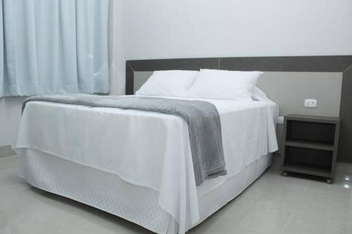a bedroom with a white bed and a night stand at Hotel Cadori in Paiçandu