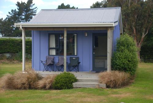 a purple tiny house with two chairs on the porch at Catlins Newhaven Holiday Park in Owaka