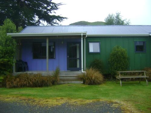 a blue and green house with a bench in the yard at Catlins Newhaven Holiday Park in Owaka