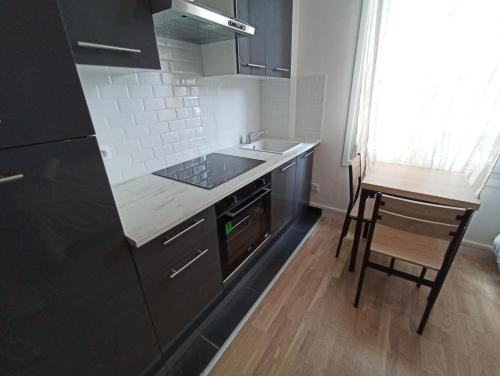 a kitchen with black cabinets and a sink and a chair at Studio cosy - Hypercentre - 20 min to Paris in Maisons-Laffitte