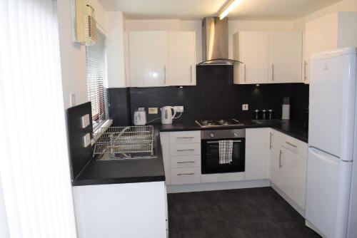 a kitchen with white cabinets and black counter tops at Kelpies Serviced Apartments- McLaughlan in Falkirk