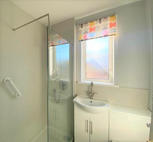 La salle de bains est pourvue d'un lavabo, d'une douche et d'une fenêtre. dans l'établissement Cliff Court Apartments, à Torquay