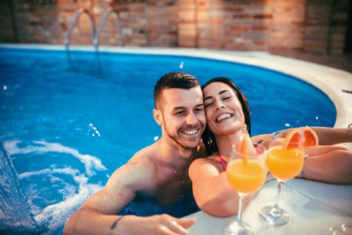 a man and woman in a swimming pool with glasses of orange juice at Etno Vila Kula in Malo Središte
