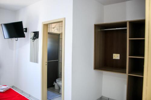 a bathroom with a toilet and a tv on a wall at Hotel Palugi in Joinville