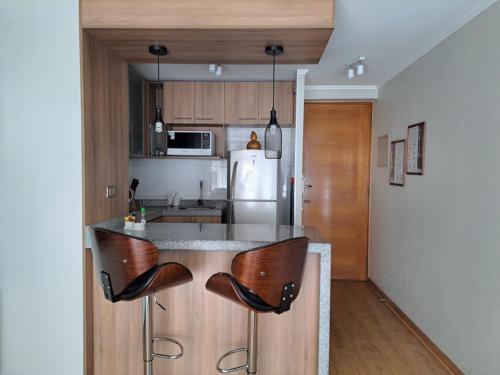 Il comprend une cuisine équipée d'un comptoir avec des chaises et d'un réfrigérateur. dans l'établissement NM ApartHotel Cochrane, à Concepción