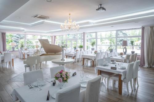 un restaurant avec des tables et des chaises blanches et un lustre dans l'établissement Hotel Europejski, à Nysa