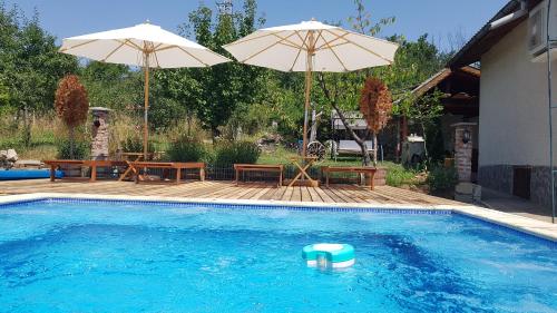 a swimming pool with two umbrellas and a table and benches at СПА къща за гости Каза Роза - Swiss Style Chalet Casa Rosa SPA Guest House in Kyustendil