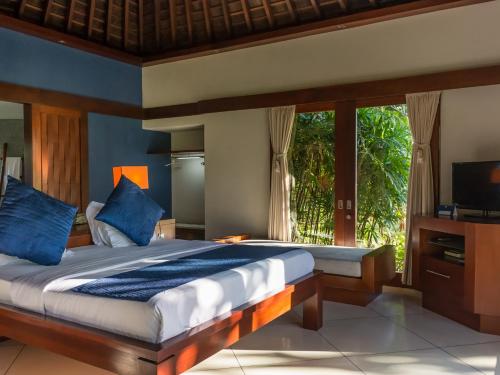 sypialnia z łóżkiem z niebieskimi poduszkami i telewizorem w obiekcie The Anandita by Elite Havens w mieście Teluknarat