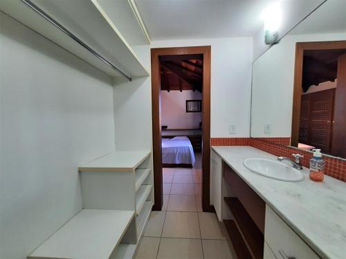 a bathroom with a sink and a mirror and a bedroom at 3Suítes, piscina e vista do mar em condomínio pé na areia - pátio compartilhado in Búzios