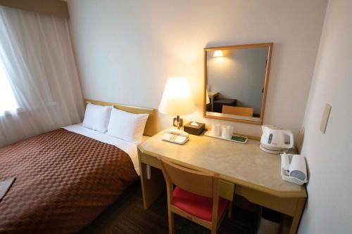 a hotel room with a bed and a desk with a mirror at Court Hotel Mito in Mito