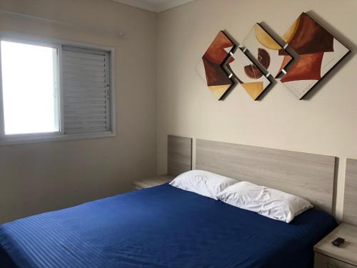 1 dormitorio con 1 cama azul y pinturas en la pared en Apartamento beira mar - Mongaguá, en Mongaguá