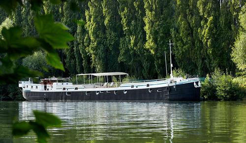 a boat floating on the water near a forest at Péniche Daphné's in Auvers-sur-Oise