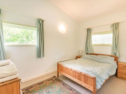a bedroom with a bed and two windows at The Log Cabin in Honiton