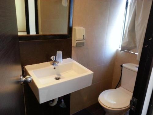 La salle de bains est pourvue d'un lavabo blanc et de toilettes. dans l'établissement L Hotel at Broadway, à Singapour