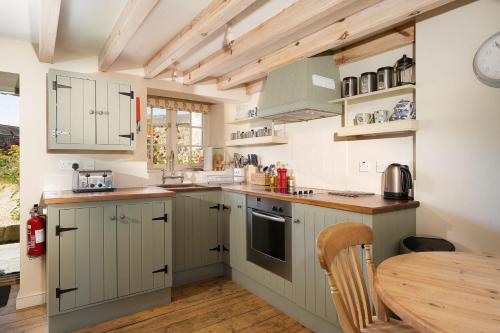 uma cozinha com armários verdes e uma mesa de madeira em Moon Cottage em Newquay