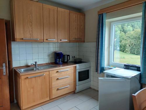 cocina con armarios de madera, fregadero y ventana en Ferienwohnung Vertatschablick en Ferlach